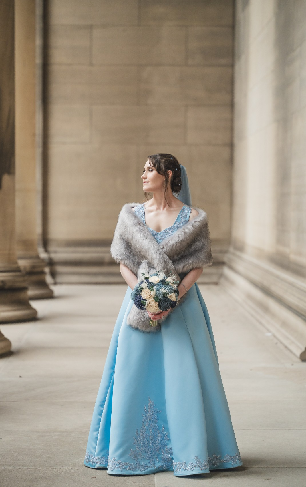 Bride in pale blue ballgown with fur wrap holding floral bouquet