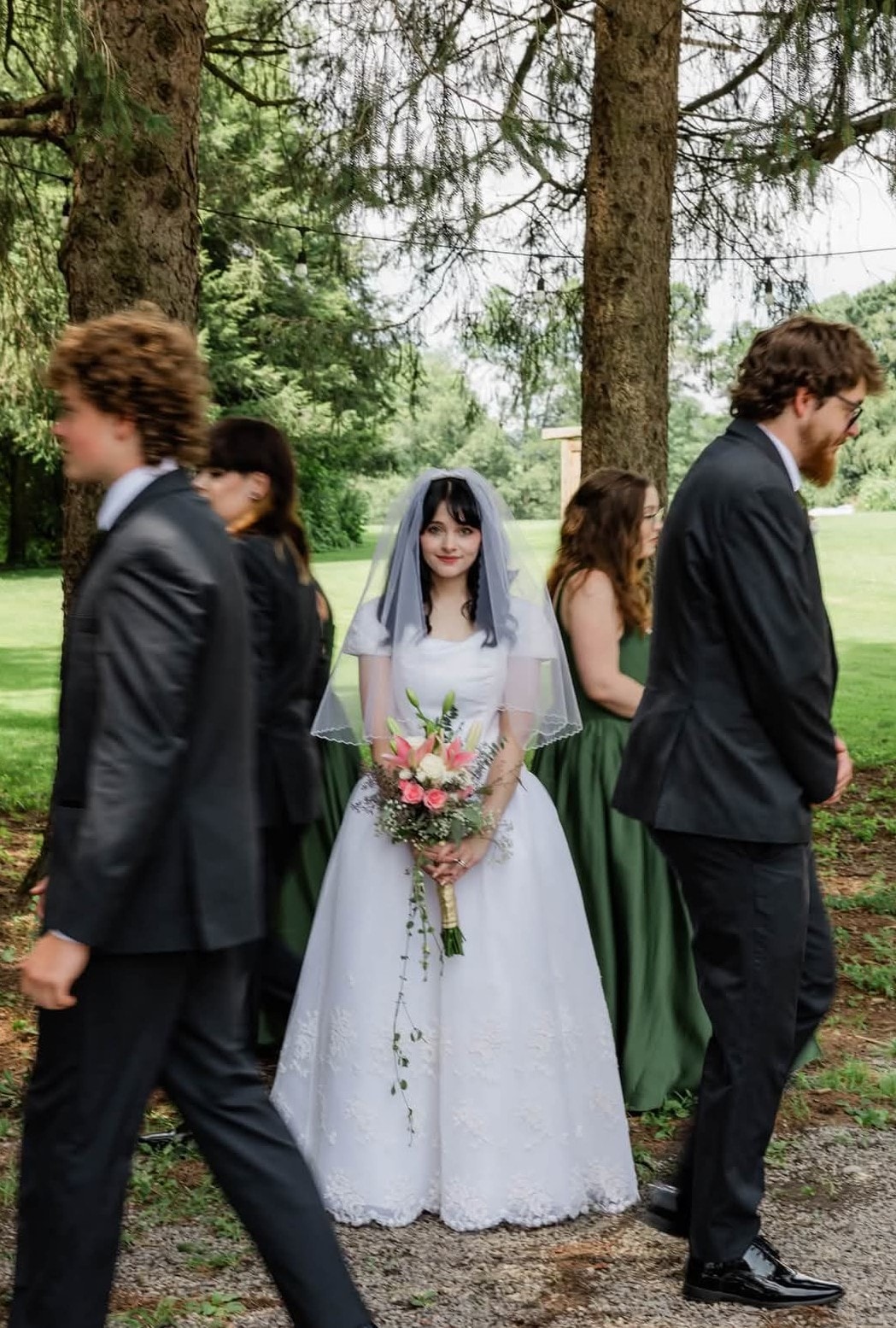 Bride in white ballgown with blue veil surrounded by wedding party outdoors