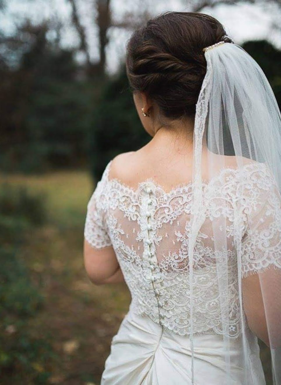 Bride showing intricate lace back detail with veil in garden
